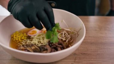 Bir fast food işletmesine yakın bir yerde siyah üniformalı büyük bir şef Japon udon çorbasını hazır malzemelerden hazırlar ve çorba döker.