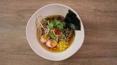 Bir restoranda, açık bir masada, Japon udon çorbası, yumurta ve erişte karışımı Japon çorbası içeren beyaz bir tabakta yakın çekim videosu.