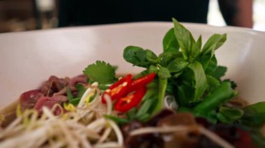 Fast food restoranının en iyi görüntüsü. Siyah üniformalı büyük bir şef Japon udon çorbasını hazırlıyor. Cımbızla son rötuşları yapıyor.