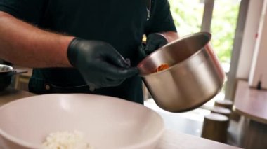 Yakın plan bir fast food işletmesinde siyah üniformalı büyük bir şef ahşap bir masada beyaz pilavı tabağa koyar.