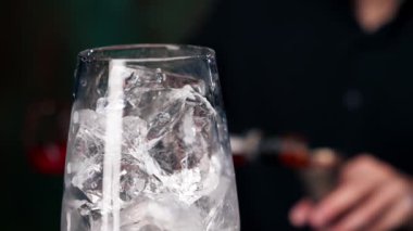 Siyah bir zemin üzerinde şarap kadehini kapatıyoruz. Camda ezilmiş buz var. Portakal rengi Aperol Spritz bir bardağa dökülüyor.