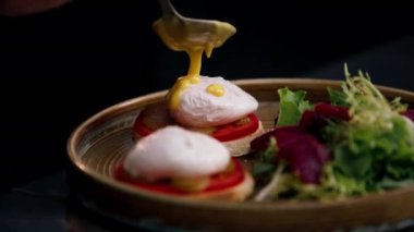 Profesyonel bir mutfakta, temiz metal bir masanın üzerinde kadın bir şef taze etle bir salata toplar ve yuvarlak ahşap bir tabakta mozzarella ile tost yapar.