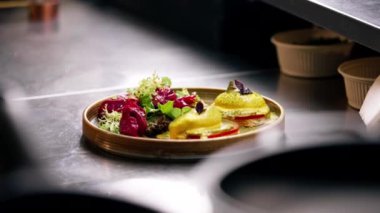 Profesyonel bir mutfakta, temiz metal bir masada, ahşap bir tabakta, domatesli ve mozzarella tostlu güzel bir salata.