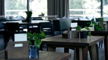 Minimalist tarzda parlak büyük bir restoran. Masada yeşil dekoru olan bir sürü ahşap masa var.