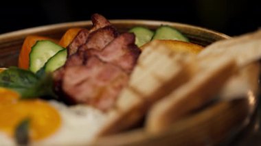 Profesyonel bir mutfakta, temiz metal bir masanın üstünde kadın bir şef yuvarlak ahşap bir tabakta İngiliz kahvaltısı toplar.