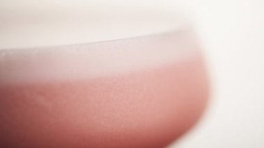 Arka planda pembe köpüklü bir şarap kadehinin makro çerçevesi. Bardakta köpüklü, susuz, alkollü, turuncu bir içecek.