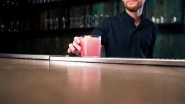Barmen elinde bir bardak dolusu taze gül kokteyli tutuyor. Ekşi ve tatlı.