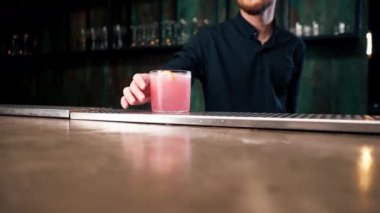 Barmen elinde bir bardak dolusu taze gül kokteyli tutuyor. Ekşi ve tatlı.