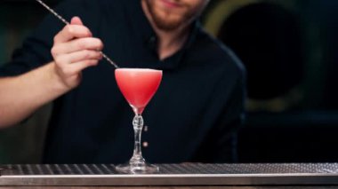 Güzel kristal bardakla kırmızı alkolik içeceği yakın plan. Adam onu pembe buğdayla süslüyor.