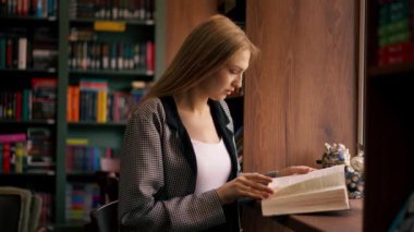 Pencerenin yanındaki bir kitapçıda güzel bir öğrenci oturmuş kitap okuyor sınavlara hazırlanıyor yeni bir kitap okuyor.