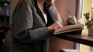 Pencerenin yanındaki bir kitapçıda güzel bir öğrenci oturmuş kitap okuyor sınavlara hazırlanıyor yeni bir kitap okuyor.