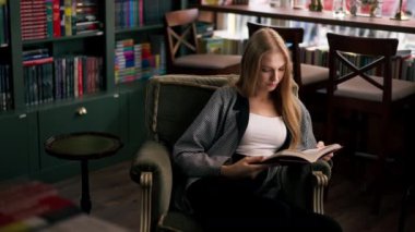 Güzel bir kitapçıda, uzun saçlı genç bir kız bir kitap akşamında boş zamanlarında kitap okuyor.