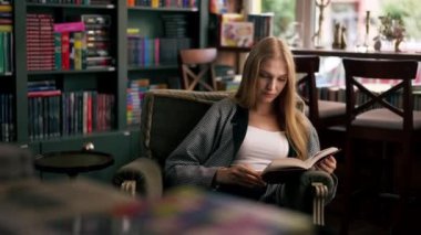 Güzel bir kitapçıda, uzun saçlı genç bir kız bir kitap akşamında boş zamanlarında kitap okuyor.
