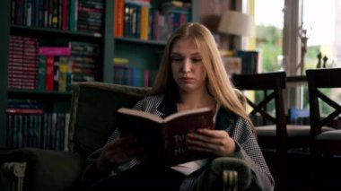 Güzel bir kitapçıda, uzun saçlı genç bir kız kitap akşamları boş zamanlarında kitap okuyor.