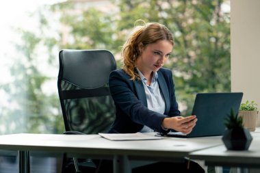 Geniş pencereli modern bir ofiste mavi gömlekli güzel bir işçi kameraya bakar genç bir patron.