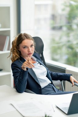 Modern bir ofiste, geniş pencereli kameraya bakın. Mavi gömlekli, dizüstü bilgisayarlı güzel bir işçi kameraya bakıyor. Genç bir patron parmağıyla işaret ediyor.