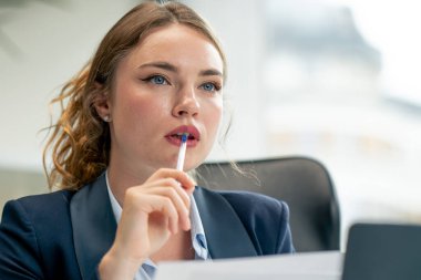 Modern bir ofise yakın büyük bir penceresi olan mavi gömlekli güzel bir işçi dizüstü bilgisayarlı genç bir patron belgelerle çalışan genç bir patron.