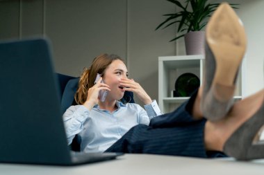 Modern bir ofiste, büyük bir penceresi olan mavi gömlekli güzel bir işçi ayaklarını masaya uzatıp çok ileri gider ve düşük verimlilik çağrısı yapar.
