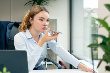 Modern bir ofiste büyük bir penceresi olan mavi gömlekli güzel bir kadın işçi masada oturur, kendini çok ileri götürür ve telefonda düşük verimlilik konuşmaları yapar.