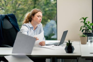 Modern bir ofiste geniş pencereli mavi gömlekli güzel bir işçi laptoplu genç bir patron belgelerle çalışıyor.