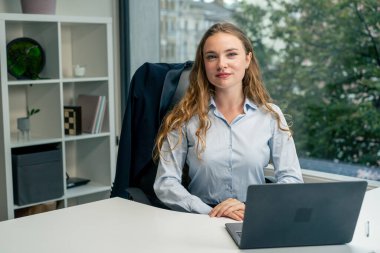 Geniş pencereli modern bir ofiste mavi gömlekli güzel bir işçi kameraya bakar, genç bir patron.