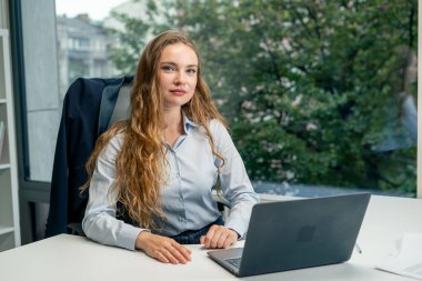 Geniş pencereli modern bir ofiste mavi gömlekli güzel bir işçi kameraya bakar, genç bir patron.