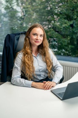 Geniş pencereli modern bir ofiste mavi gömlekli güzel bir işçi kameraya bakar, genç bir patron.