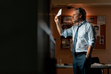 Dedektiflik bürosunda gömlekli ve kravatlı orta yaşlı bir dedektif büyüteçle inceler kanıt inceler suçlu fotofit güzergahı suçlu tahtası ipuçlarını inceler