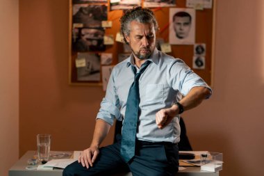 Dedektiflik bürosunda gömlekli ve kravatlı orta yaşlı bir müfettiş kol saatindeki saate bakarak cevap arıyor.