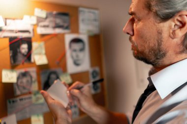 Dedektiflik bürosu gömlekli ve kravatlı orta yaşlı araştırmacı. Suçlu fotofit güzergahı suç duyuru panosu notlarını kalem ile ararken cinayet silahlarını arıyor.