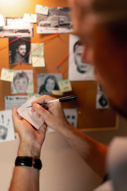 Dedektiflik bürosu gömlekli ve kravatlı orta yaşlı araştırmacı. Suçlu fotofit güzergahı suç duyuru panosu notlarını kalem ile ararken cinayet silahlarını arıyor.