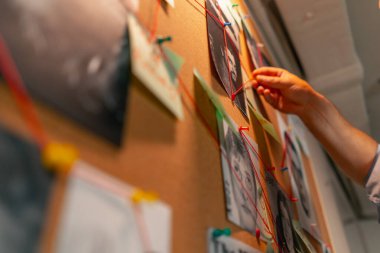 Dedektif ofisini kapatın. Gömlekli ve kravatlı orta yaşlı araştırmacı gerçeği bulmak için ipucu panosunun yanında duruyor.