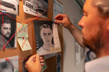 Dedektif ofisini kapatın. Gömlekli ve kravatlı orta yaşlı araştırmacı gerçeği bulmak için ipucu panosunun yanında duruyor.