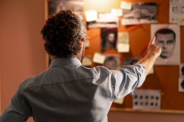 Dedektif ofisi gömlekli ve kravatlı araştırmacı gerçeği bulmak için ipucu panosunun yanında duruyor.