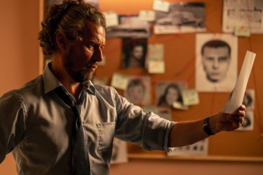 Dedektiflik bürosunda gömlekli ve kravatlı orta yaşlı bir dedektif büyüteçle inceler kanıt inceler suçlu fotofit güzergahı suçlu tahtası ipuçlarını inceler