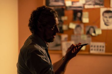 Yakın plan dedektiflik bürosu gömlekli ve kravatlı araştırmacı. Telefonda konuşarak gerçeği bulmak için ipucu panosunun yanında duruyor.