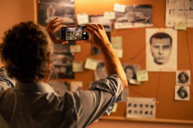 Dedektif bürosu gömlekli ve kravatlı dedektifi bulmaca çözmede ipucu panosunun yanında duruyor.