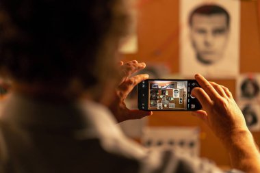 Dedektif bürosu gömlekli ve kravatlı dedektifi bulmaca çözmede ipucu panosunun yanında duruyor.