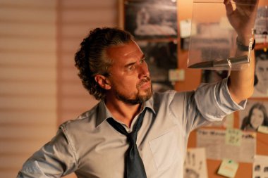 Dedektiflik bürosu gömlekli ve kravatlı orta yaşlı bir dedektif ziplock 'ta cinayet silahını inceliyor.