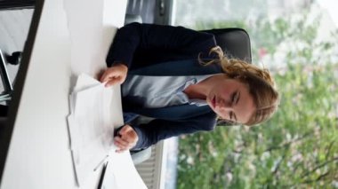 Modern bir ofiste, geniş pencereli bir dikey video dizüstü bilgisayarı olan güzel bir işçi belgelerle çalışan genç bir patron.