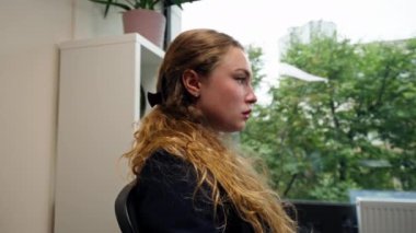 Modern bir ofiste büyük bir penceresi olan mavi gömlekli, dizüstü bilgisayarlı güzel bir bayan işçi masada oturur sıkıcı bir iş başını dik tutar ve günün sonunu bekler.