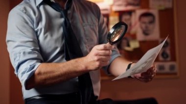Dedektiflik bürosunda gömlekli ve kravatlı orta yaşlı bir dedektif büyüteçle inceler kanıt inceler suçlu fotofit güzergahı suçlu tahtası ipuçlarını inceler
