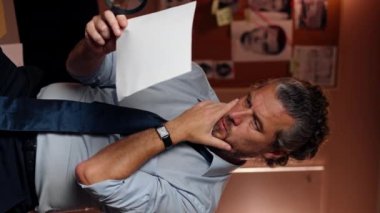 Dedektiflik bürosundaki dikey video. Gömlek ve kravat giyen orta yaşlı bir dedektif büyüteçle inceler. Kanıt inceler.