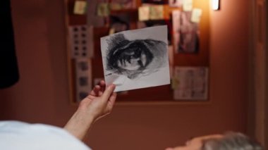 Dedektiflik bürosundaki dikey video. Gömlekli ve kravatlı orta yaşlı bir müfettiş büyüteçle inceler. Kanıt, suçlunun fotofit güzergahını bulmak için ipuçlarını inceler.