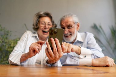 Yaşlı insanlar bir masada oturup sosyal ağları izliyorlar komik videolar, mutlu yaşlı çiftler, güzel anılar, yaşlılıktan sonra sıcak duygular destek oluyor.