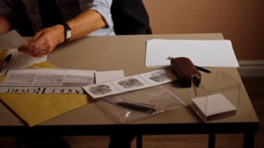 Dedektiflik bürosunun gömlekli ve kravatlı orta yaşlı dedektifinin yakın plan fotoğrafı. Masada oturmuş büyüteçle robot resmi inceliyor.