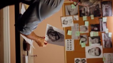 Dedektiflik bürosundaki dikey video. Gömlekli ve kravatlı orta yaşlı bir müfettiş büyüteçle inceler. Kanıt, suçlunun fotofit güzergahını bulmak için ipuçlarını inceler.