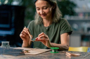 in a large green workshop, a thin woman with green hair at a large table, green glass petals, working with a soldering iron, design cutting out to shape clipart