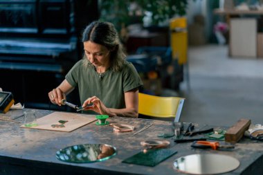Yeşil saçlı bir kadın üzerinde büyük yeşil bir atölyede dekoratif çiçekler yaratıyor ayna el sanatlarında metal bant dekoru ile çalışıyor.
