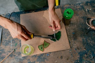 Yeşil saçlı bir kadın üzerinde büyük yeşil bir atölyede dekoratif çiçekler yaratıyor ayna el sanatlarında metal bant dekoru ile çalışıyor.